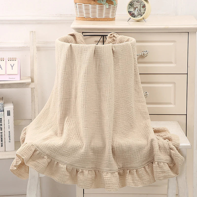 Couverture bébé en coton Beige avec volants délicats, drapée sur un panier en osier, offrant une texture douce et respirante, idéale pour le confort et la chaleur de votre bébé, dans un décor bohème avec vase artistique et fleurs séchées en arrière-plan.