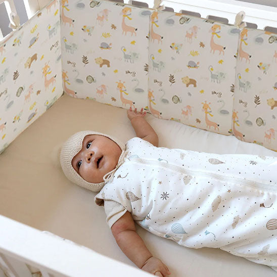 Tour de lit bébé à motifs d'animaux fixé à un lit dans lequel un bébé est allongé