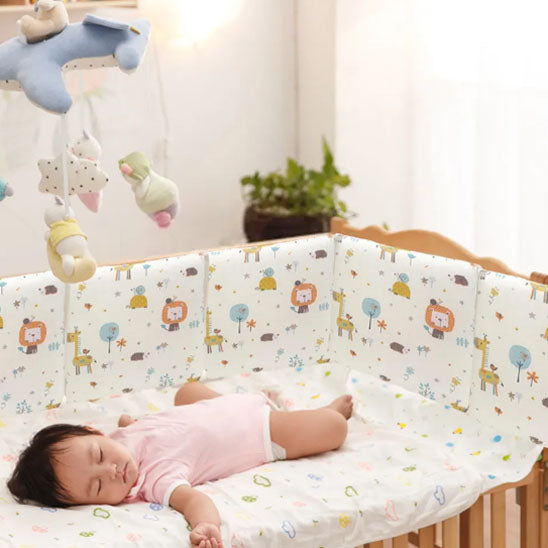 Tour de lit bébé à motif d'animaux fixé à un lit dans lequel un bébé dort paisiblement