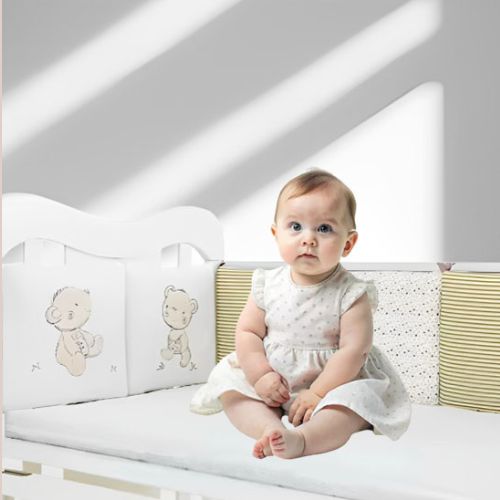 Dans un lit , bébé assis avec tour de lit rembourré, motifs oursons et rayures, assurant confort et sécurité.