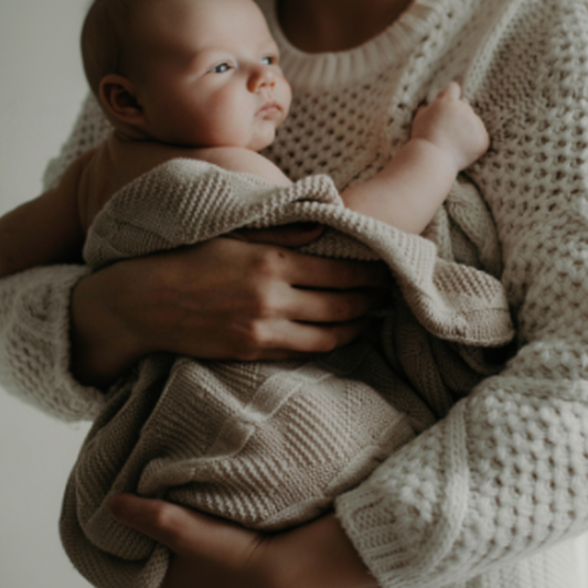 Parent tenant un nouveau-né enveloppé dans une couverture bébé en tricot beige