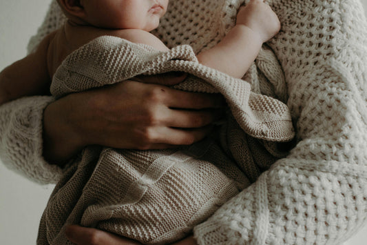 Couverture bébé en maille tricotée beige en coton doux, dans les bras réconfortants de maman, moment cocooning chaleureux, linge de lit bébé naturel, accessoire indispensable pour chambre bébé et cadeau de naissance.