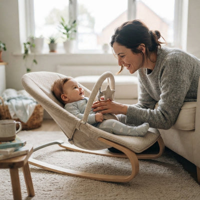 Transat bébé ergonomique et moderne, une maman sourit à son nouveau-né en body blanc installé confortablement dans le transat en bois et tissu clair au salon avec lumière naturelle douce.