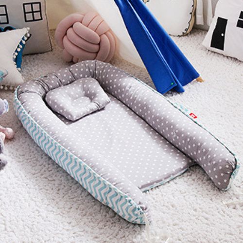 Couffin bébé confortable et design en tissu gris à étoiles blanches avec des rebords rembourrés et un coussin assorti, doté d'un motif chevron bleu sur les côtés, idéal pour offrir un espace douillet et sécurisé aux nouveau-nés, détaché et installé dans une chambre décorée avec des coussins et un tipi bleu en arrière-plan.