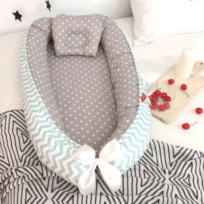 Couffin bébé confortable avec matelas gris à motifs d'étoiles blanches, rebords rembourrés et contour en tissu chevron bleu clair et blanc, agrémenté d'un joli nœud blanc, idéal pour offrir un cocon douillet et sécurisé au nourrisson, posé sur un lit avec une planche en bois décorée de cerises et d'une bougie.