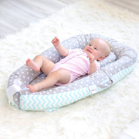 Couffin bébé confortable et sécurisé en tissu gris à motifs d'étoiles et chevrons bleu clair, posé sur un tapis blanc moelleux, avec un nourrisson souriant vêtu d'un body rose allongé à l'intérieur, jouant et levant les bras et les jambes.