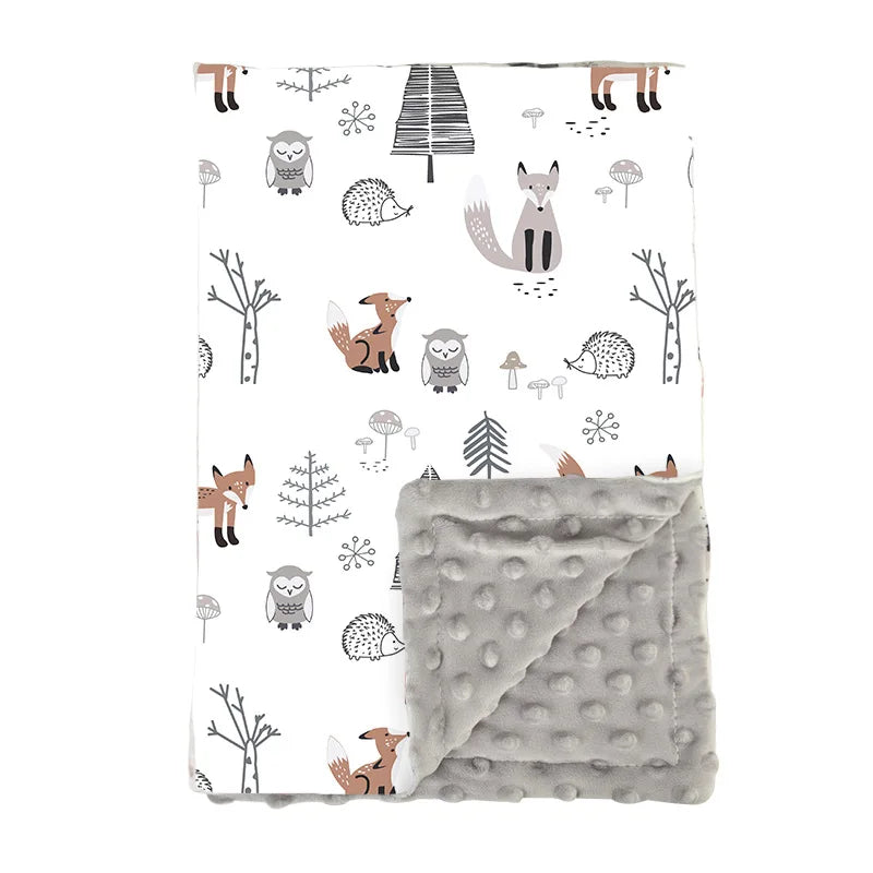 Couverture bébé douce et réversible avec un motif forêt comprenant des renards, un hibou, un hérisson, des arbres stylisés et des champignons sur fond blanc, et un côté en tissu minky gris à pois en relief.