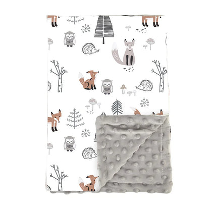 Couverture bébé douce et réversible avec un motif forêt comprenant des renards, un hibou, un hérisson, des arbres stylisés et des champignons sur fond blanc, et un côté en tissu minky gris à pois en relief.