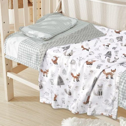 Couverture bébé évolutive qui s'adapte à la croissance de l'enfant, disposée sur un lit à barreaux en bois, avec un motif forestier représentant des renards, des hérissons, des arbres et autres éléments naturels, accompagnée d'un coussin gris à carreaux et d'un tissu gris texturé.