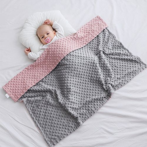 Couverture bébé en tissu doux à pois en relief, bicolore gris et rose, enveloppant partiellement un nourrisson allongé sur un drap blanc, tête posée sur un coussin et tétine en bouche, créant une routine du coucher rassurante et apaisante.