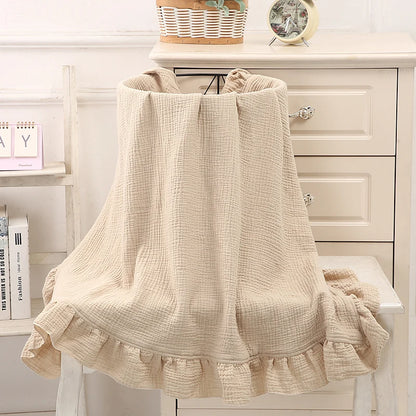 Couverture bébé  en coton Beige avec volants délicats, drapée sur un panier en osier, offrant une texture douce et respirante, idéale pour le confort et la chaleur de votre bébé, dans un décor bohème avec vase artistique et fleurs séchées en arrière-plan.