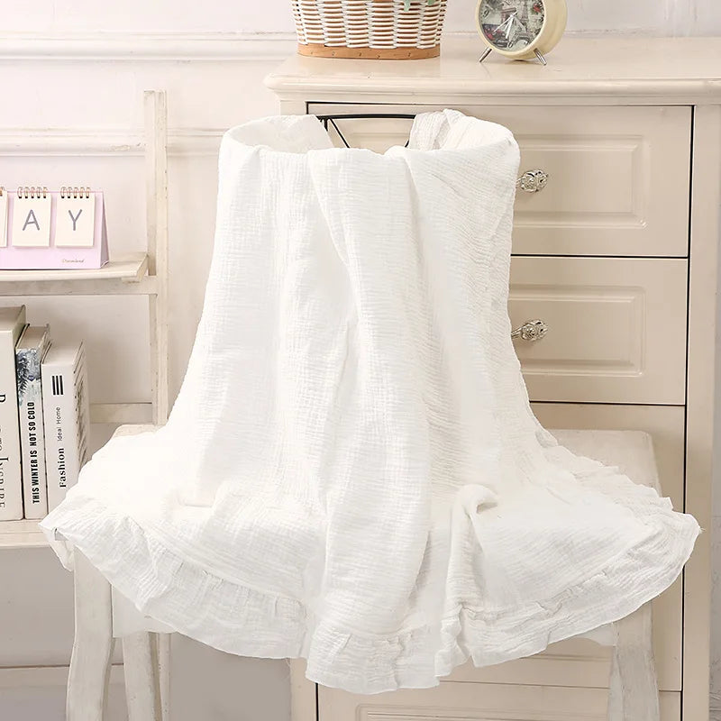 Couverture bébé  en coton Blanc avec volants délicats, drapée sur un panier en osier, offrant une texture douce et respirante, idéale pour le confort et la chaleur de votre bébé, dans un décor bohème avec vase artistique et fleurs séchées en arrière-plan.