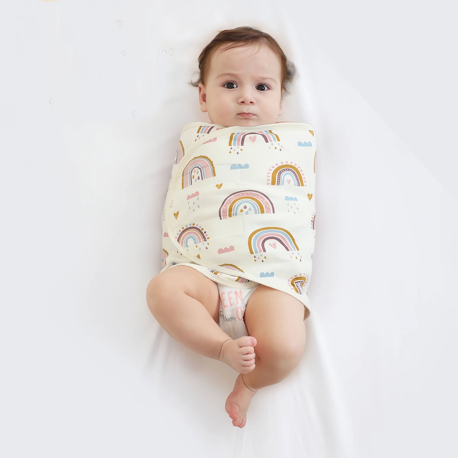 Couverture emmaillotage bébé motif arc-en-ciel enveloppant un nouveau-né pour un sommeil apaisé et sécurisé avec fermeture velcro pratique.
