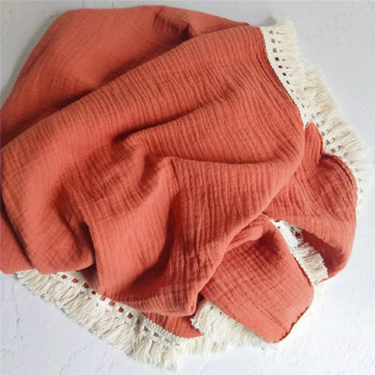Plaid bébé en mousseline orange avec franges en dentelle bohème, idéal pour envelopper votre enfant de douceur et apporter une touche élégante à sa chambre.