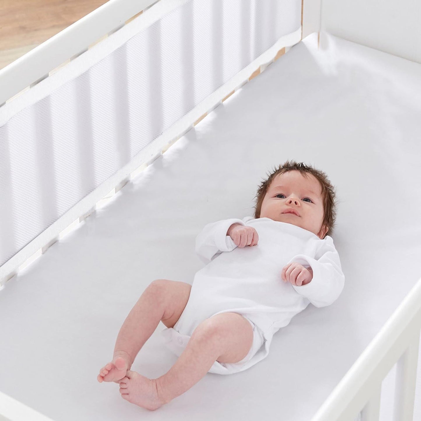 Un nourrisson confortablement installé dans un berceau équipé d’un tour de lit respirant blanc, conçu pour garantir sécurité et bien-être.