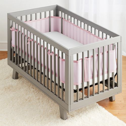 Tour de lit respirant rose, offrant un côté enveloppant, installé dans un lit vide, visible dans une chambre au décor simple
