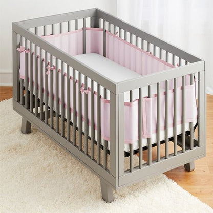 Tour de lit respirant rose, offrant un côté enveloppant, installé dans un lit vide, visible dans une chambre au décor simple
