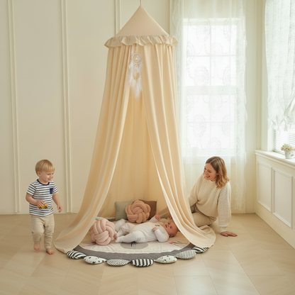 Ciel de lit bébé beige créant un espace de jeu douillet au sol avec des peluches et un tapis arc-en-ciel.