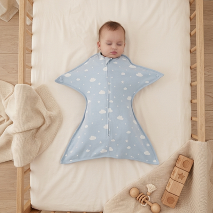 Gigoteuse bébé d'emmaillotage bleue avec motif nuages et étoiles sur un bébé endormi dans un berceau en bois.