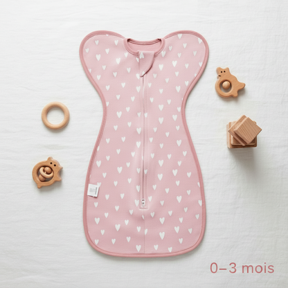 Gigoteuse d'emmaillotage rose, taille 0-3 mois, présentée à plat avec des jouets en bois.