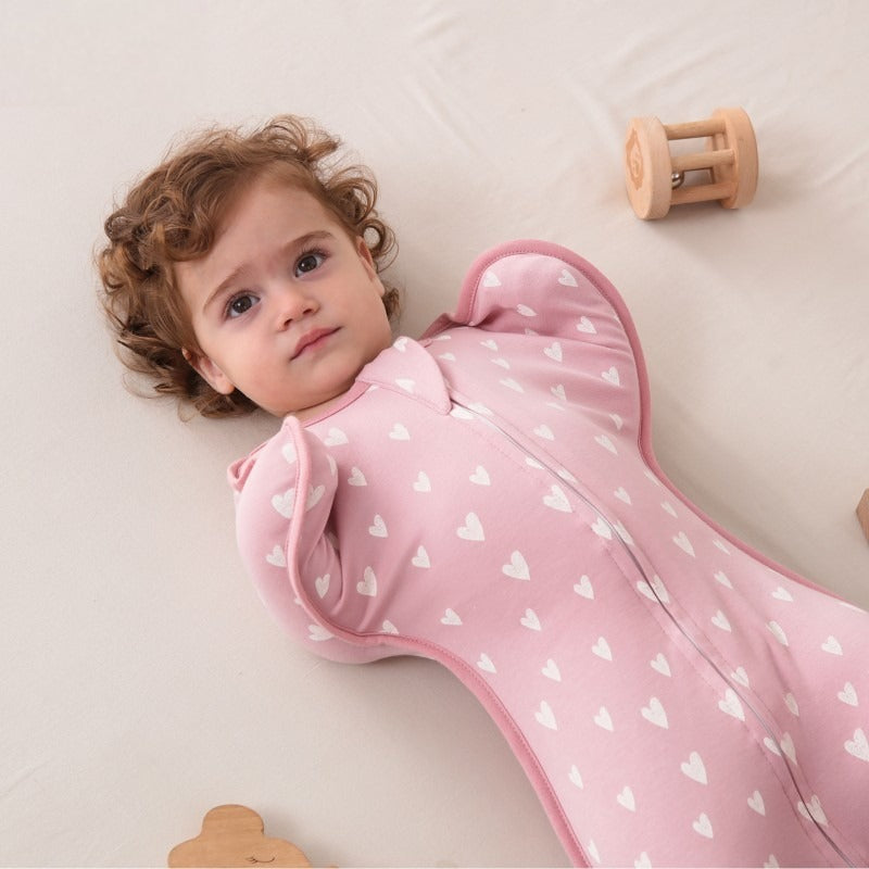 Gigoteuse d'emmaillotage rose pour bébé, vue de dessus, posée sur un lit.