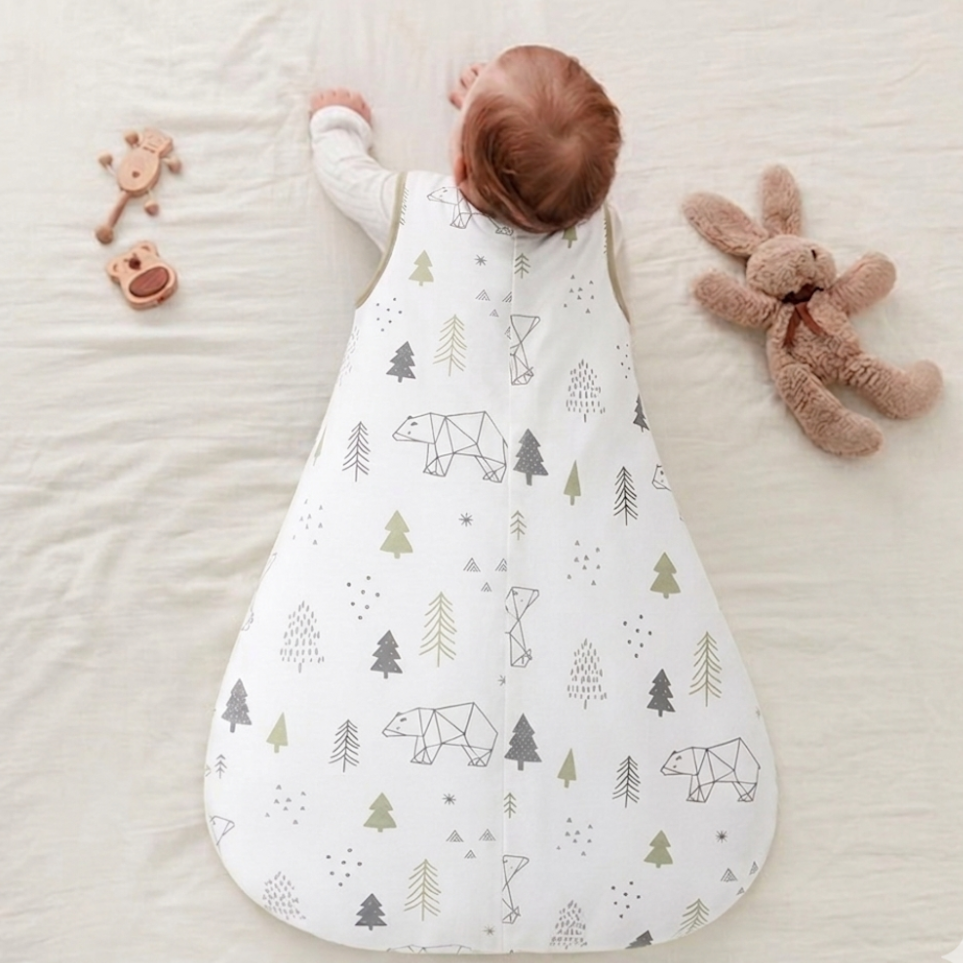 Gigoteuse bébé verte et blanche vue de dos, posée sur un drap avec un doudou à côté.