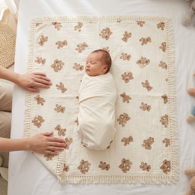lange bébé étalé à plat montrant la méthode d'emmaillotage d'un nourrisson endormi au milieu du tissu.
