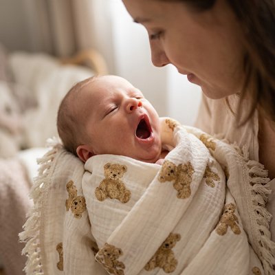 lange bébé en coton respirant enveloppant un nourrisson qui bâille blotti contre sa maman.