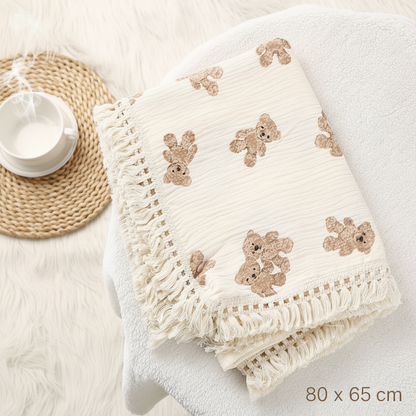 lange bébé imprimé oursons plié élégamment sur une chaise en tissu blanc à côté d'un sous-verre. 80cm x 65cm