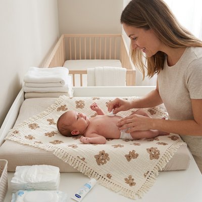 lange bébé disposé sur un matelas à langer pendant qu'une maman s'occupe de son nourrisson.