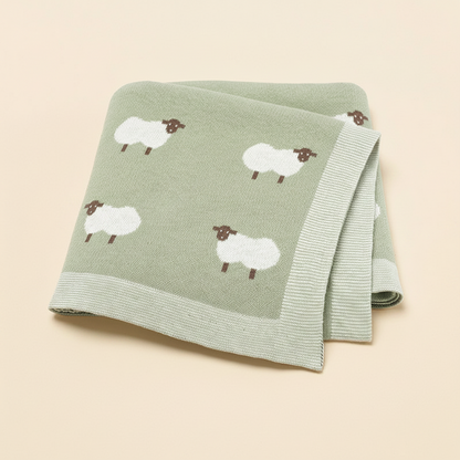 Lange bébé vert sauge aux motifs de moutons blancs, plié sur un fond neutre pour catalogue produit.