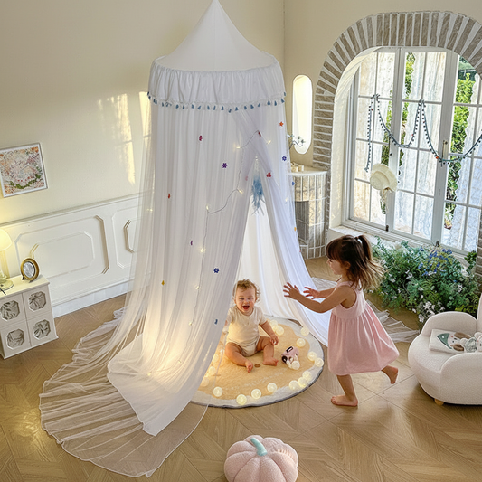 Moustiquaire lit bébé baldaquin blanc style princesse avec étoiles et pompons colorés, chambre enfant lumineuse.