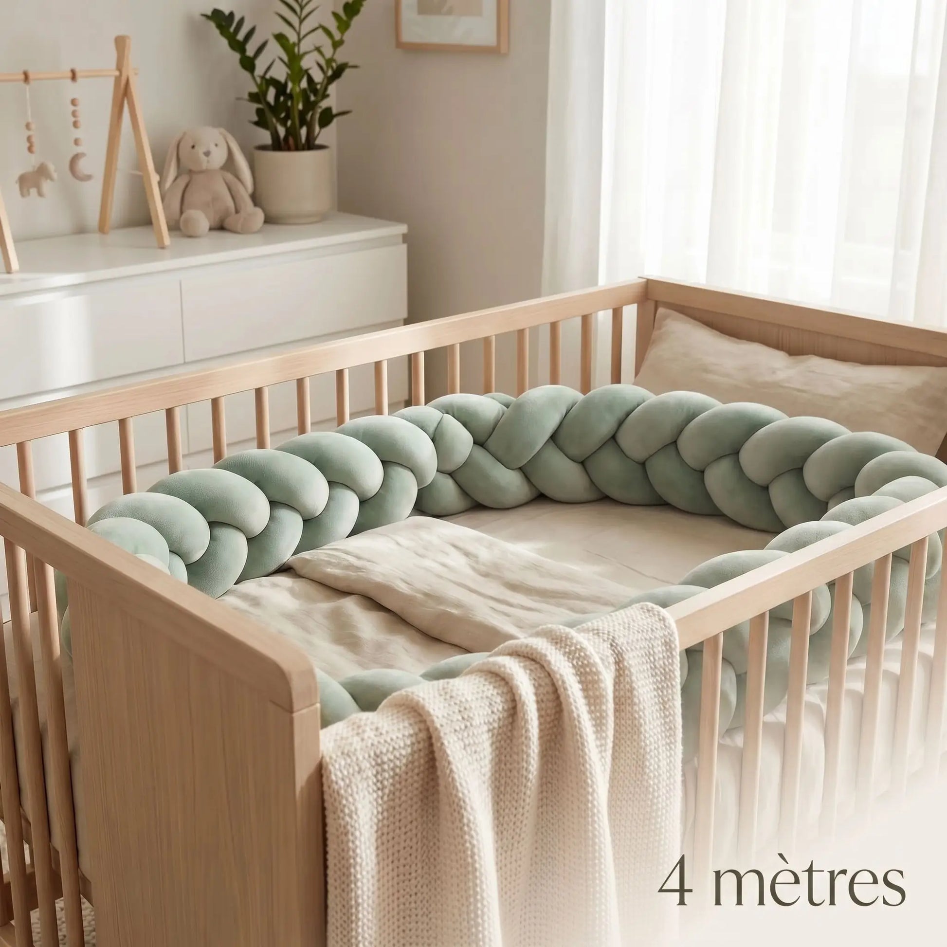 Réducteur de lit tressé de 4 mètres de long en velours vert sauge installé tout autour d'un lit à barreaux pour bébé.