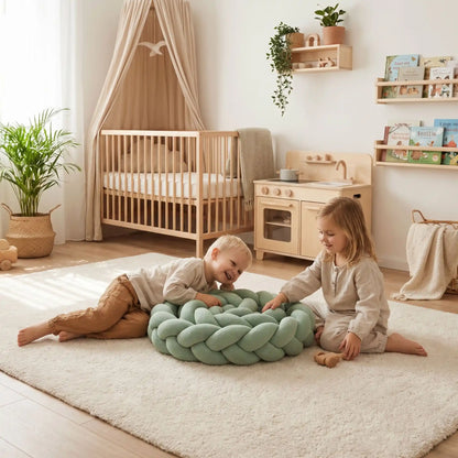 Réducteur de lit tressé de couleur vert sauge utilisé comme coussin de jeu par deux jeunes enfants dans une chambre d'enfant lumineuse au style scandinave.