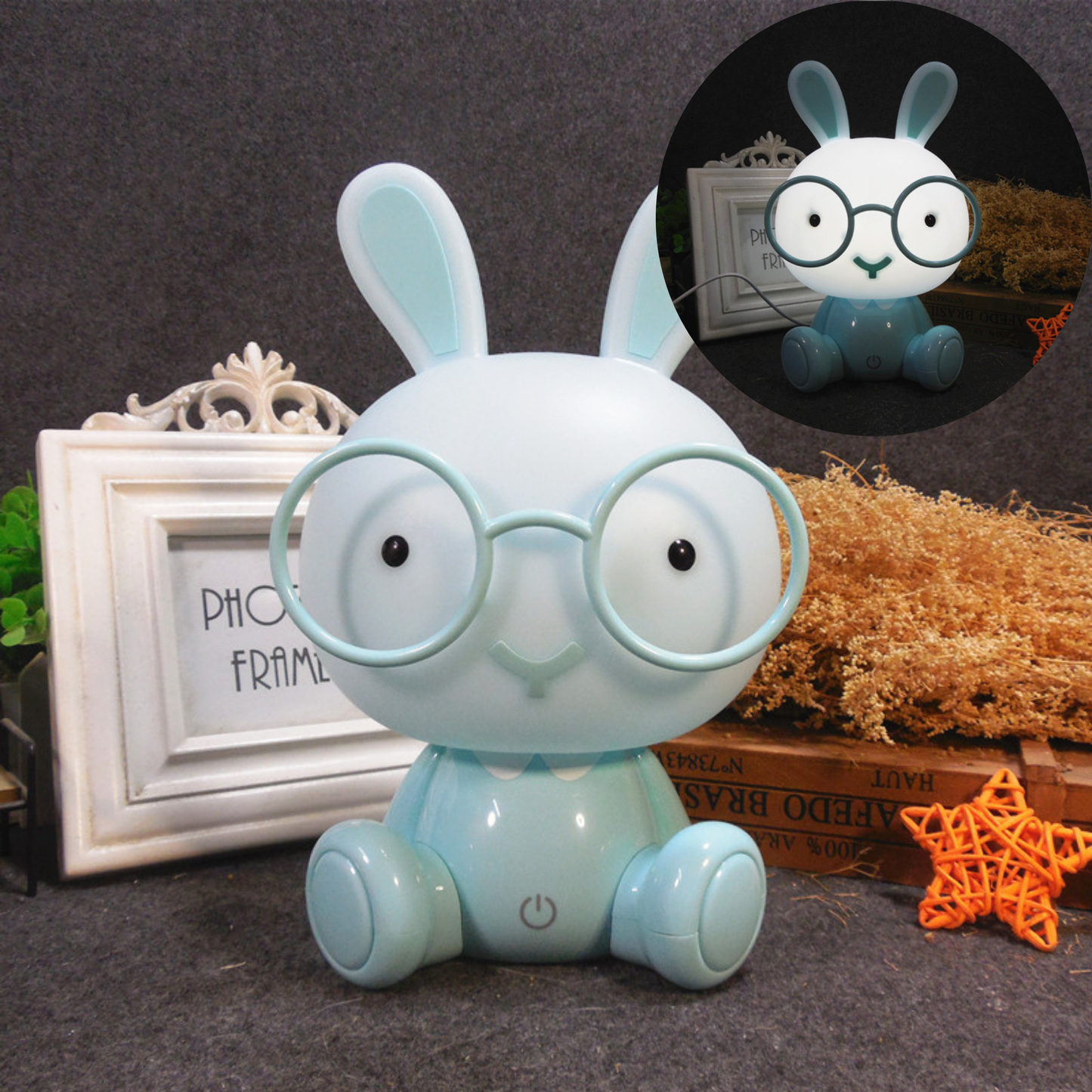 Veilleuse lapin bleue avec lunettes posée sur une table à côté d'un cadre photo blanc et d'une étoile décorative orange.