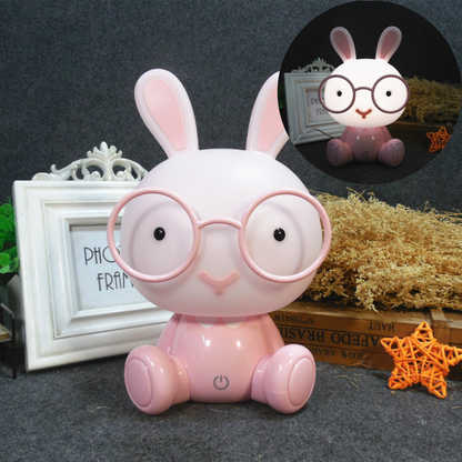 Veilleuse lapin rose avec lunettes présentée comme un objet de décoration poétique avec un cadre blanc et une étoile.