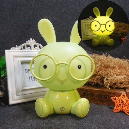 Veilleuse lapin verte lumineuse installée sur un meuble en bois à côté d'accessoires décoratifs de chambre d'enfant.